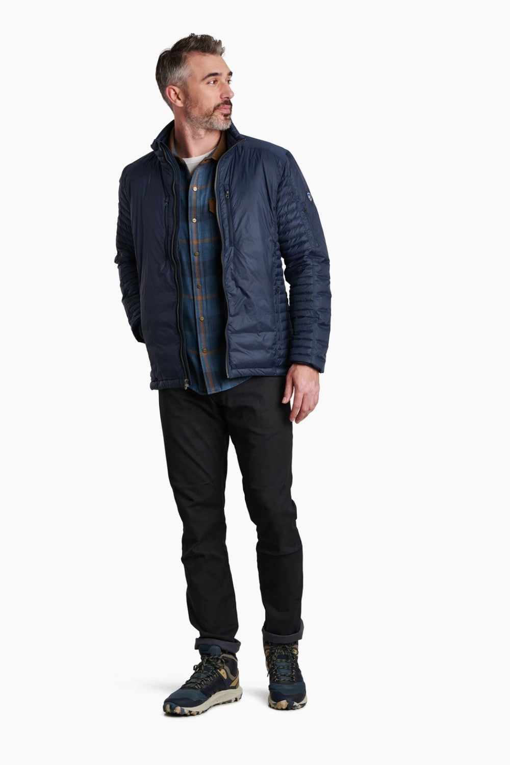 Man wearing a blue quilted jacket, plaid shirt, black pants, and hiking boots on a white background