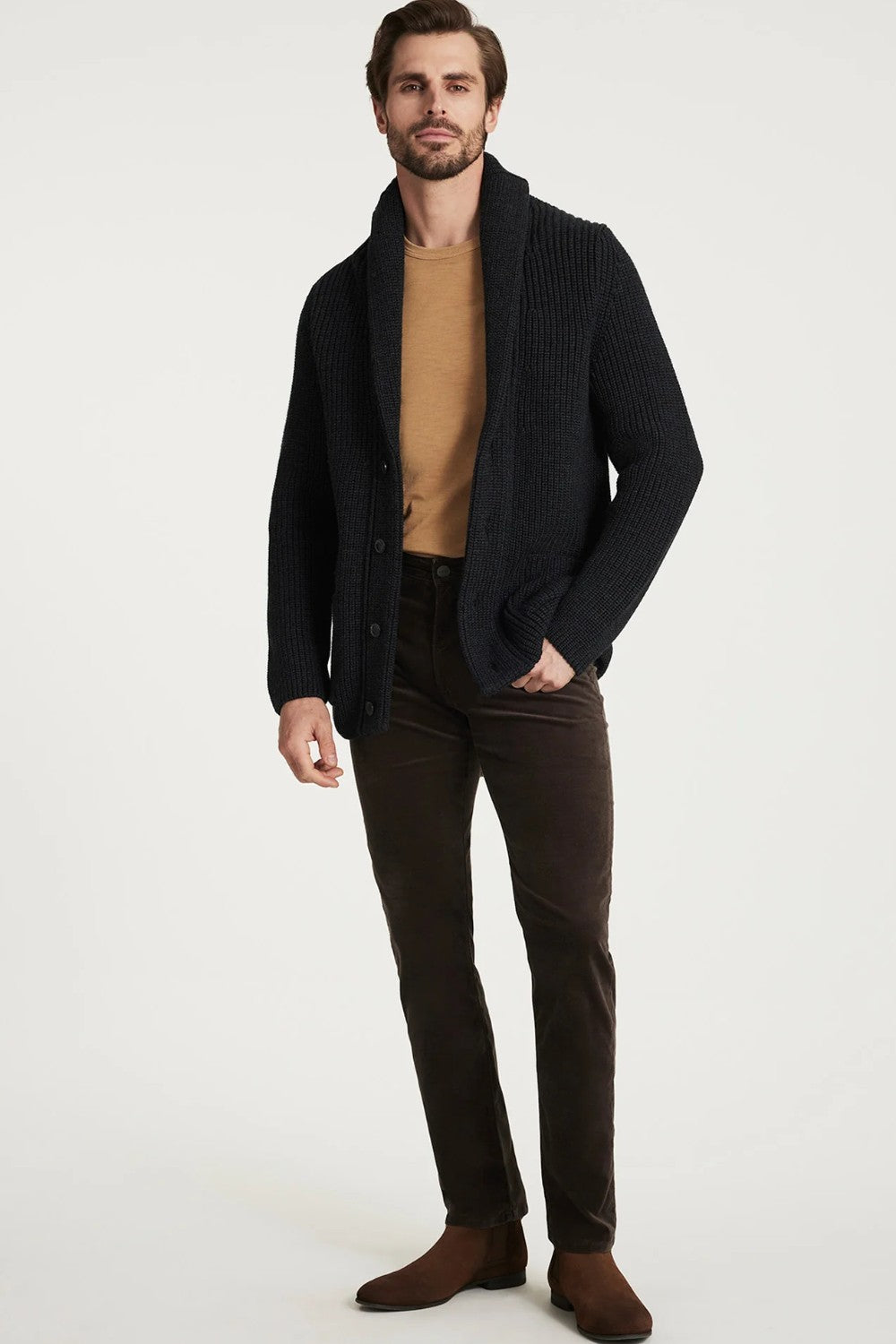 Man wearing a black cardigan, brown shirt, and dark pants on a white background