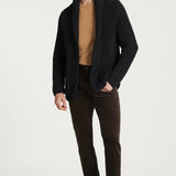 Man wearing a black cardigan, brown shirt, and dark pants on a white background