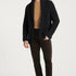 Man wearing a black cardigan, brown shirt, and dark pants on a white background