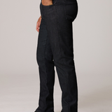 A side-profile view of a person wearing dark indigo slim-fit jeans, a white t-shirt, and black leather boots against a light gray studio background.
