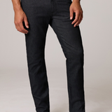 A man wearing slim-fit dark charcoal gray jeans, a white t-shirt, and black leather boots, standing against a light gray studio background.