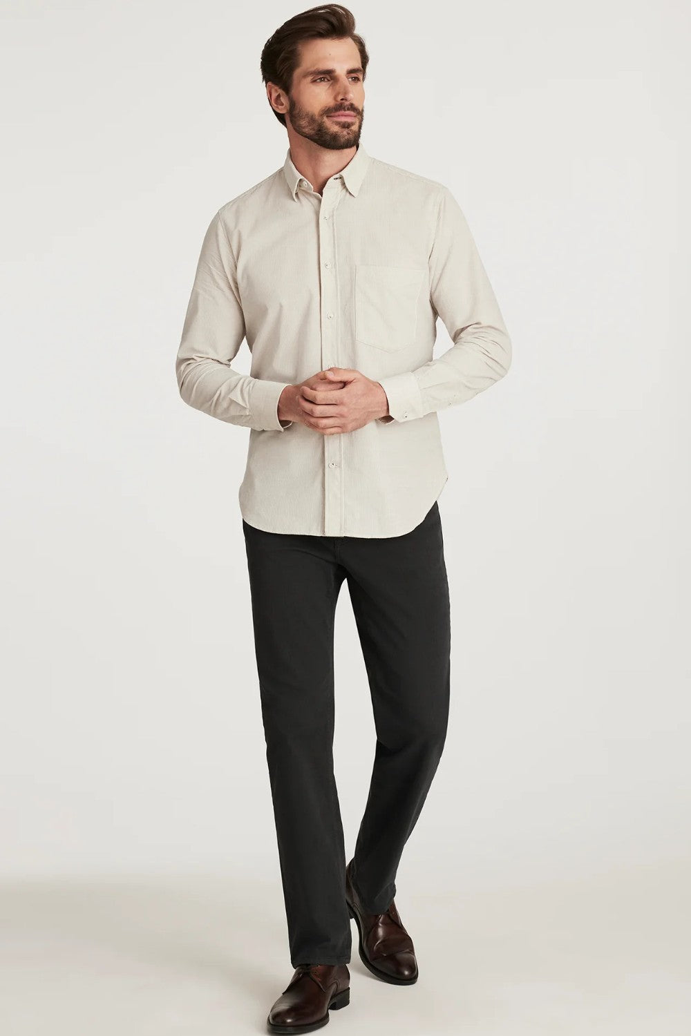 Man wearing a light-colored dress shirt and dark pants on a white background