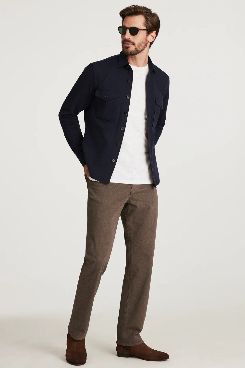 Man wearing a navy jacket, white shirt, brown pants, and sunglasses on a white background