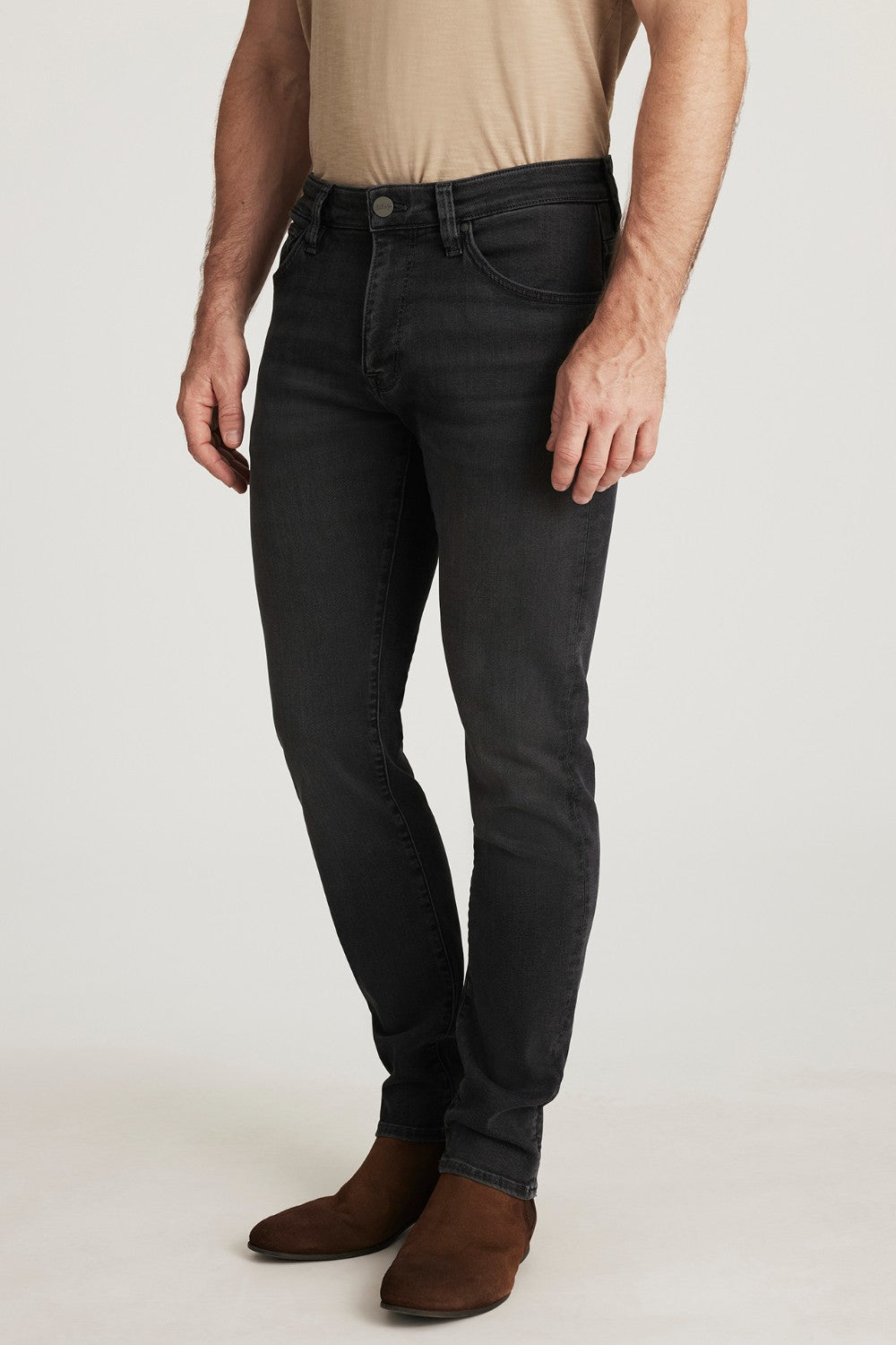 Person wearing black jeans and brown shoes on a white background