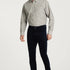 Man wearing a light gray button-up shirt, dark blue jeans, and brown shoes on a white background