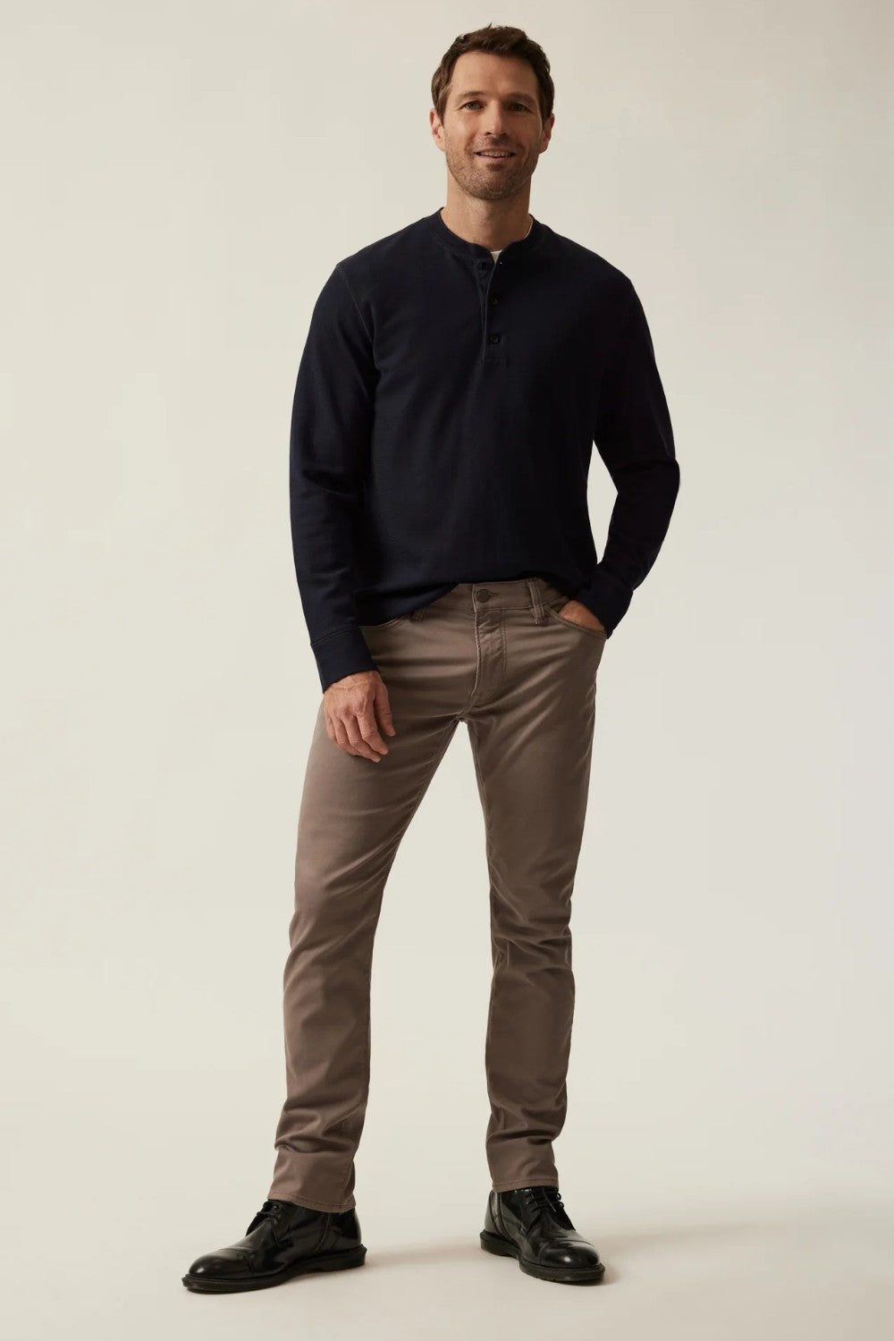 Man wearing a dark sweater and brown pants on a plain background