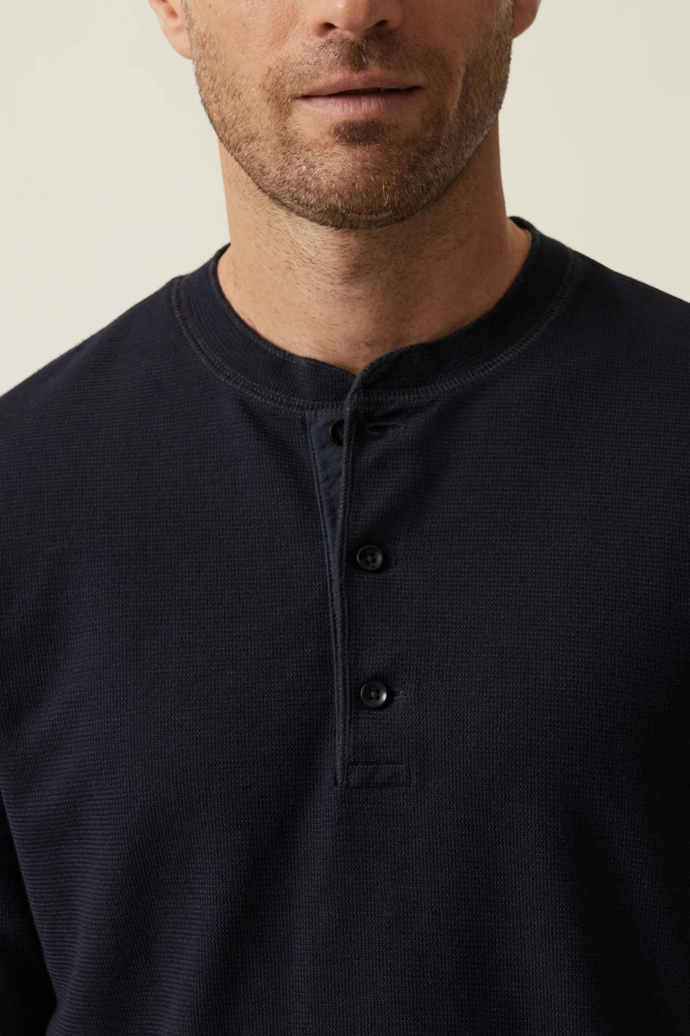 Man wearing a black henley shirt against a neutral background