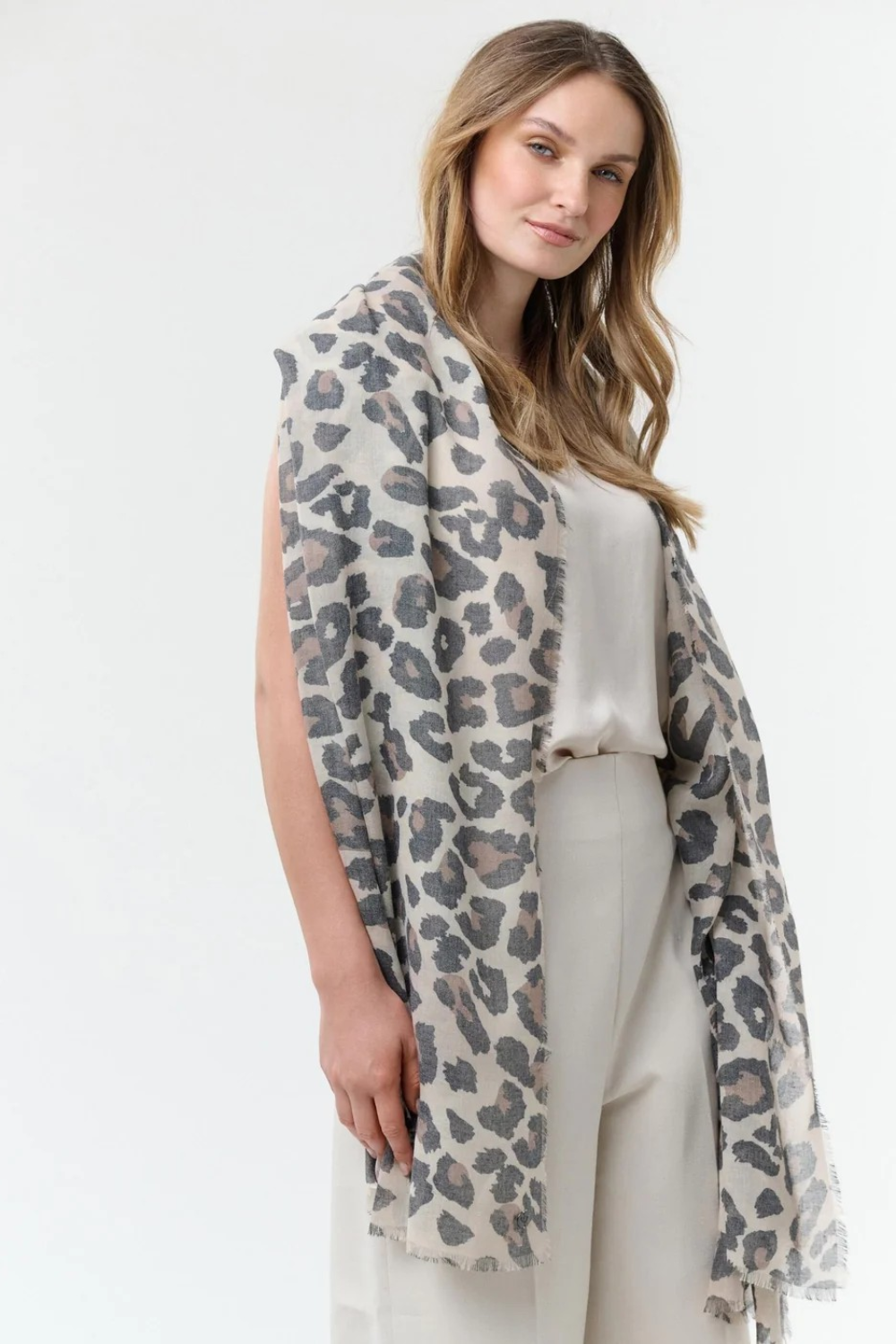 Woman modelling a leopard print scarf with a cream coloured top and bottom photographed against a light background.