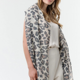 Woman modelling a leopard print scarf with a cream coloured top and bottom photographed against a light background.