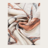Close up of a cream coloured scarf with a brown and grey equestrian print photographed on a light background.