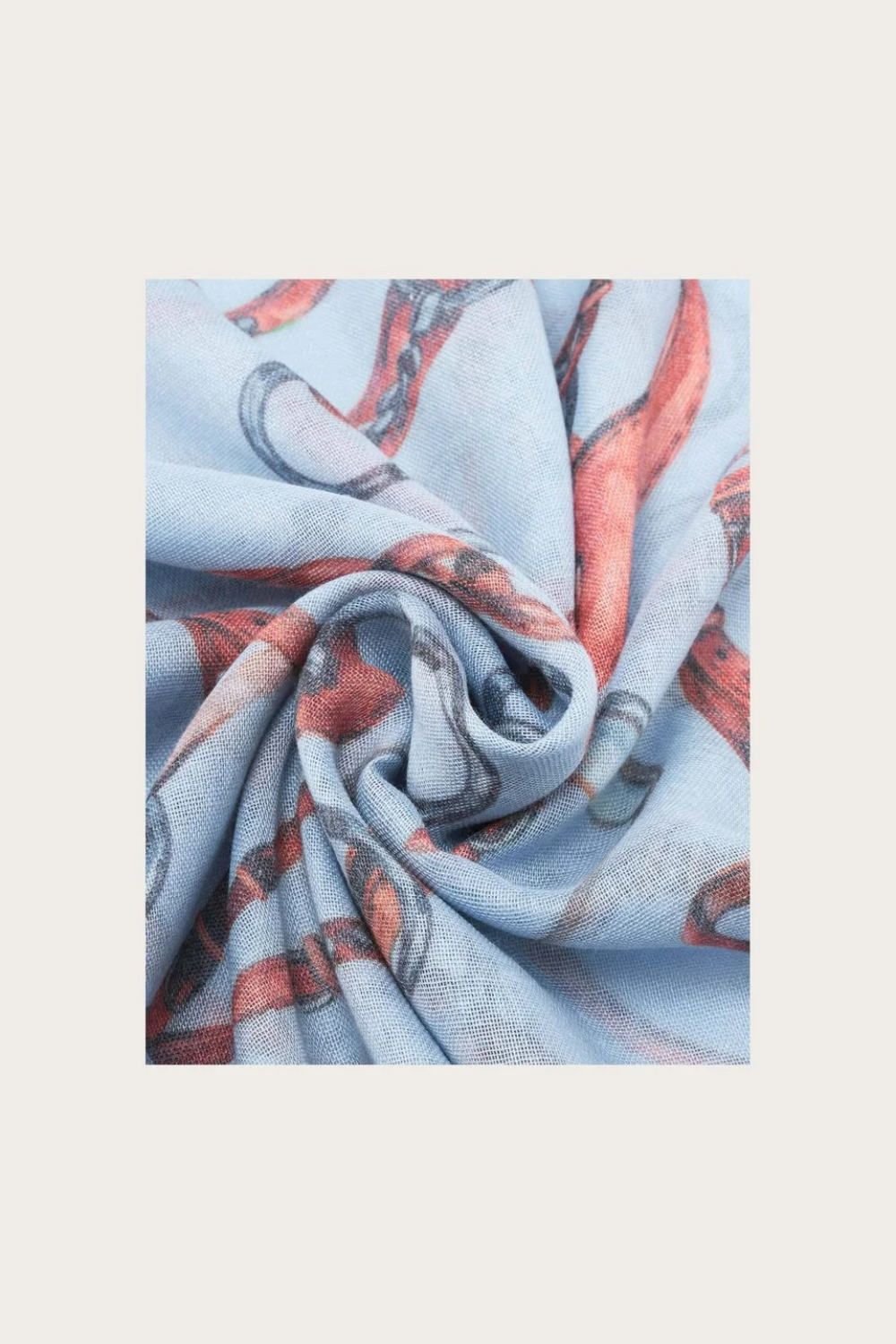 Close up of a blue coloured scarf with a brown and grey equestrian print photographed on a light background.