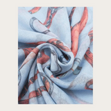 Close up of a blue coloured scarf with a brown and grey equestrian print photographed on a light background.