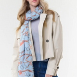 Woman modelling a blue coloured scarf with a brown and grey equestrian print, a blue top, blue jeans and a cream jacket, photographed on a light background.