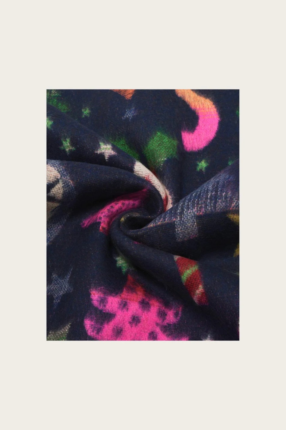 A close-up of a dark navy fabric with a colorful abstract pattern of pink, green, orange, and white star-like shapes, styled in a spiral fold on a light beige background.