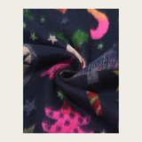 A close-up of a dark navy fabric with a colorful abstract pattern of pink, green, orange, and white star-like shapes, styled in a spiral fold on a light beige background.