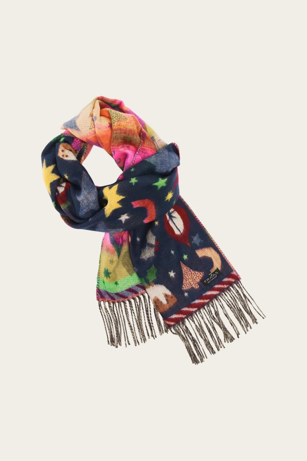 A multicolor patterned scarf with fringe, featuring a navy blue base with whimsical illustrations of stars and Christmas motifs, shown on a light beige background.