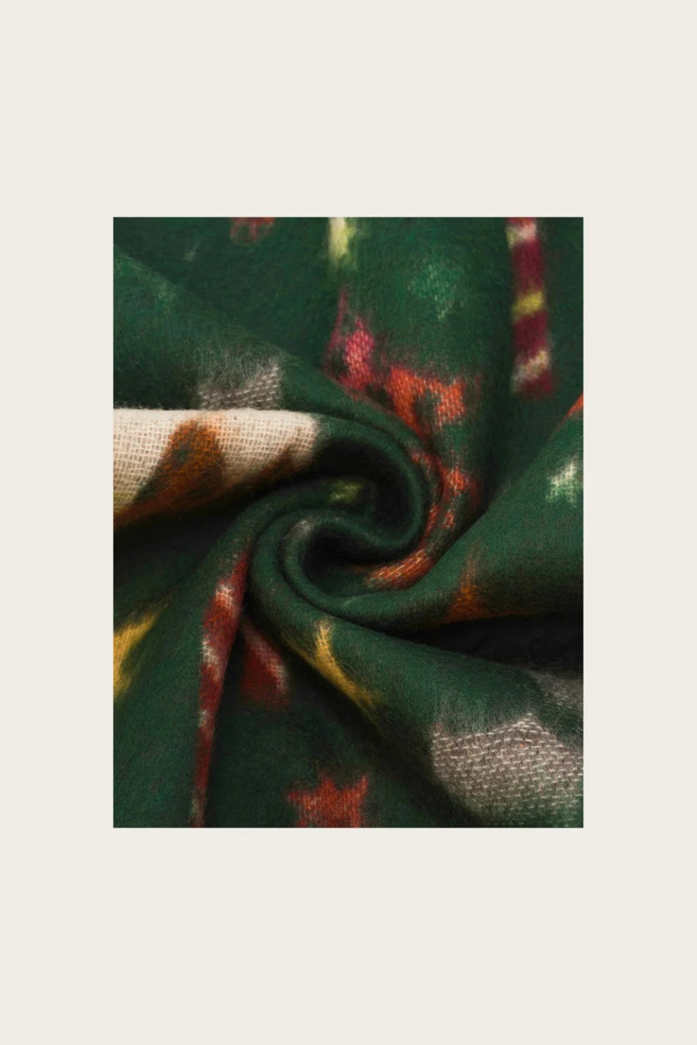 A close-up of a dark green patterned fabric swirled into a spiral, showing a textured weave with abstract red, orange, yellow, and cream motifs on a light beige background.
