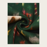 A close-up of a dark green patterned fabric swirled into a spiral, showing a textured weave with abstract red, orange, yellow, and cream motifs on a light beige background.
