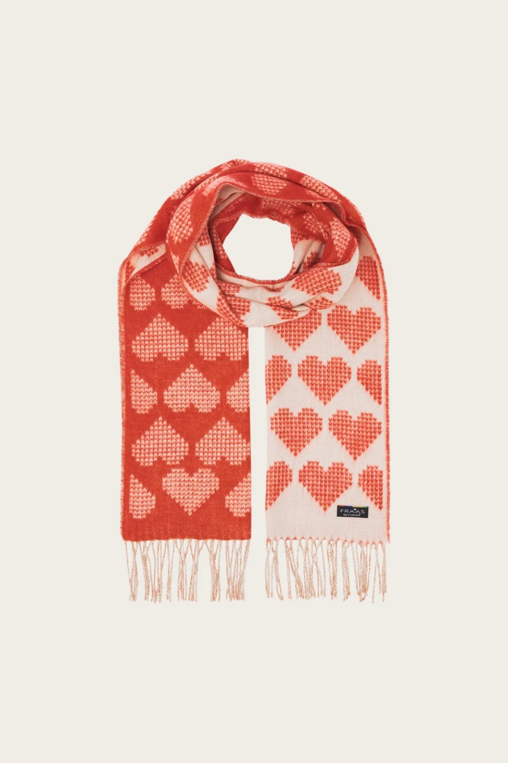 A red and cream heart printed scarf with fringe photographed on a light background.