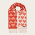A red and cream heart printed scarf with fringe photographed on a light background.