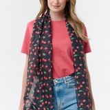 Woman modelling a black base scarf with a cherry print  on a red t-shirt with blue jeans on a light background.