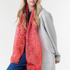 Woman modelling a red paisley scarf with a black top, blue jeans, and a grey coat, photographed on a light background.