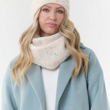 Woman modelling a cream toque with multi coloured flecks, with a matching scarf, a cream sweater and blue coat  photographed on a light background.