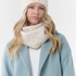 Woman modelling a cream toque with multi coloured flecks, with a matching scarf, a cream sweater and blue coat  photographed on a light background.
