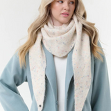 Woman modelling a cream scarf with multi coloured flecks, with a cream sweater and blue coat, photographed on a light background.