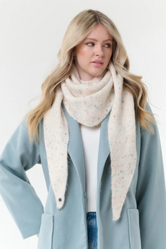 Woman modelling a cream scarf with multi coloured flecks, with a cream sweater and blue coat, photographed on a light background.