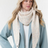 Woman modelling a cream scarf with multi coloured flecks, with a cream sweater and blue coat, photographed on a light background.