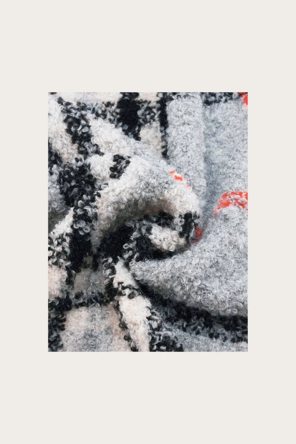 Close up of a grey, black and orange plaid scarf photographed on a light background.