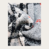 Close up of a grey, black and orange plaid scarf photographed on a light background.