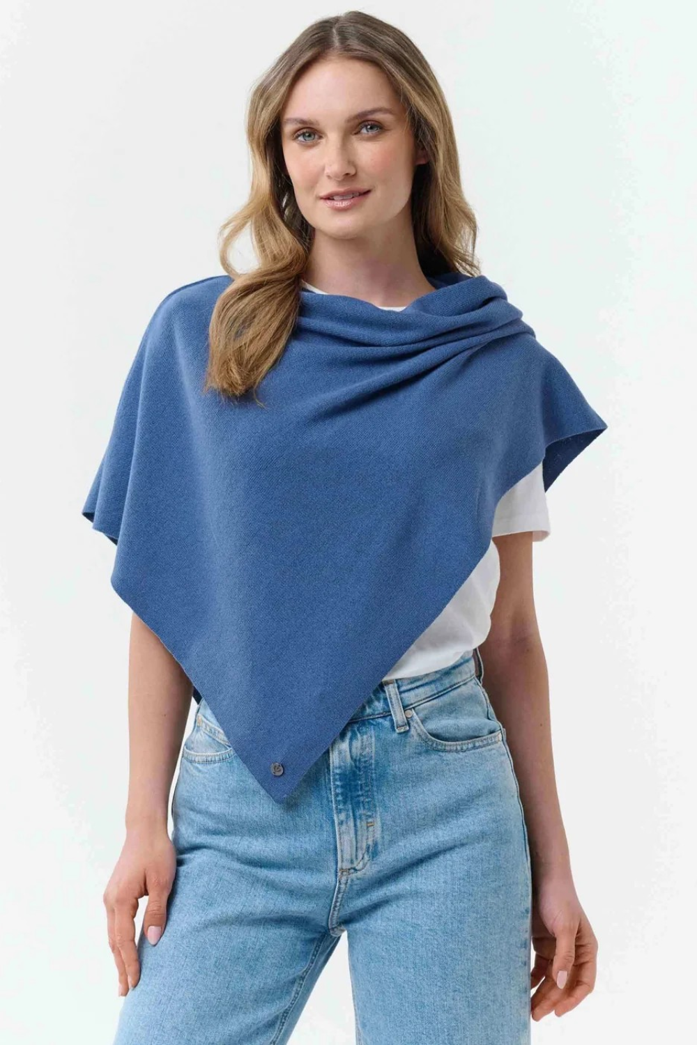 Woman modelling a blue poncho with a white t-shirt and blue jeans, against light background.