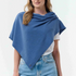 Woman modelling a blue poncho with a white t-shirt and blue jeans, against light background.
