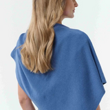 Woman, shown from behind, modelling a blue poncho, with blue jeans, against light background.