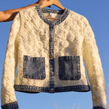 White lace jacket with denim accents on a hanger against a blue sky.