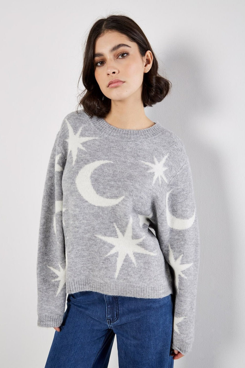 Woman wearing a gray sweater with star and moon patterns against a white background