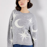Woman wearing a gray sweater with star and moon patterns against a white background