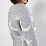 Person wearing a gray sweater with star and moon designs on a plain background