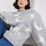 Woman wearing a gray sweater with star and moon patterns against a plain background