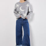 Woman wearing a gray sweater with star and moon patterns and blue jeans on a white background
