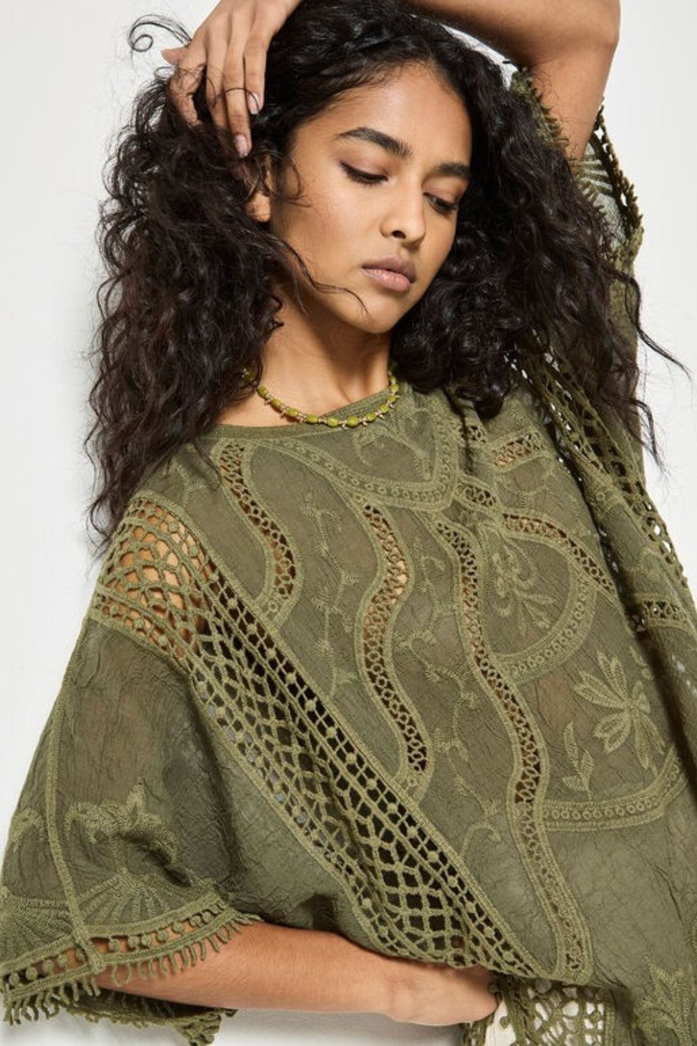 Woman wearing a green embroidered poncho against a white background