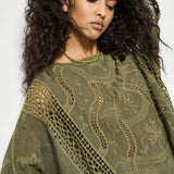 Woman wearing a green embroidered poncho against a white background