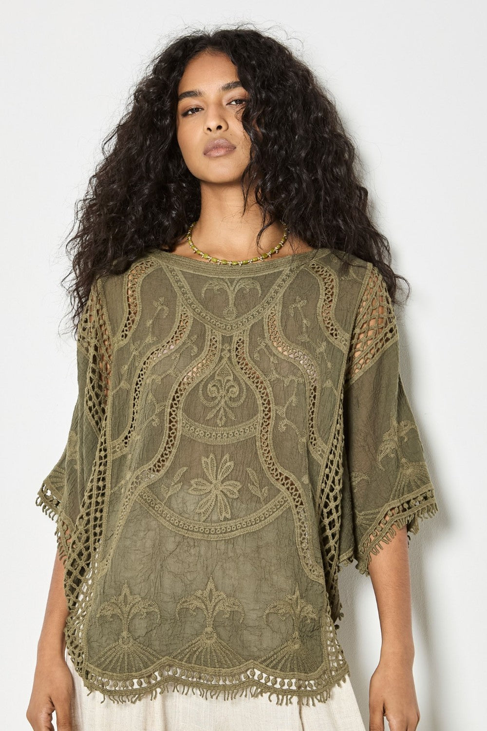 Woman wearing a green embroidered top against a white background