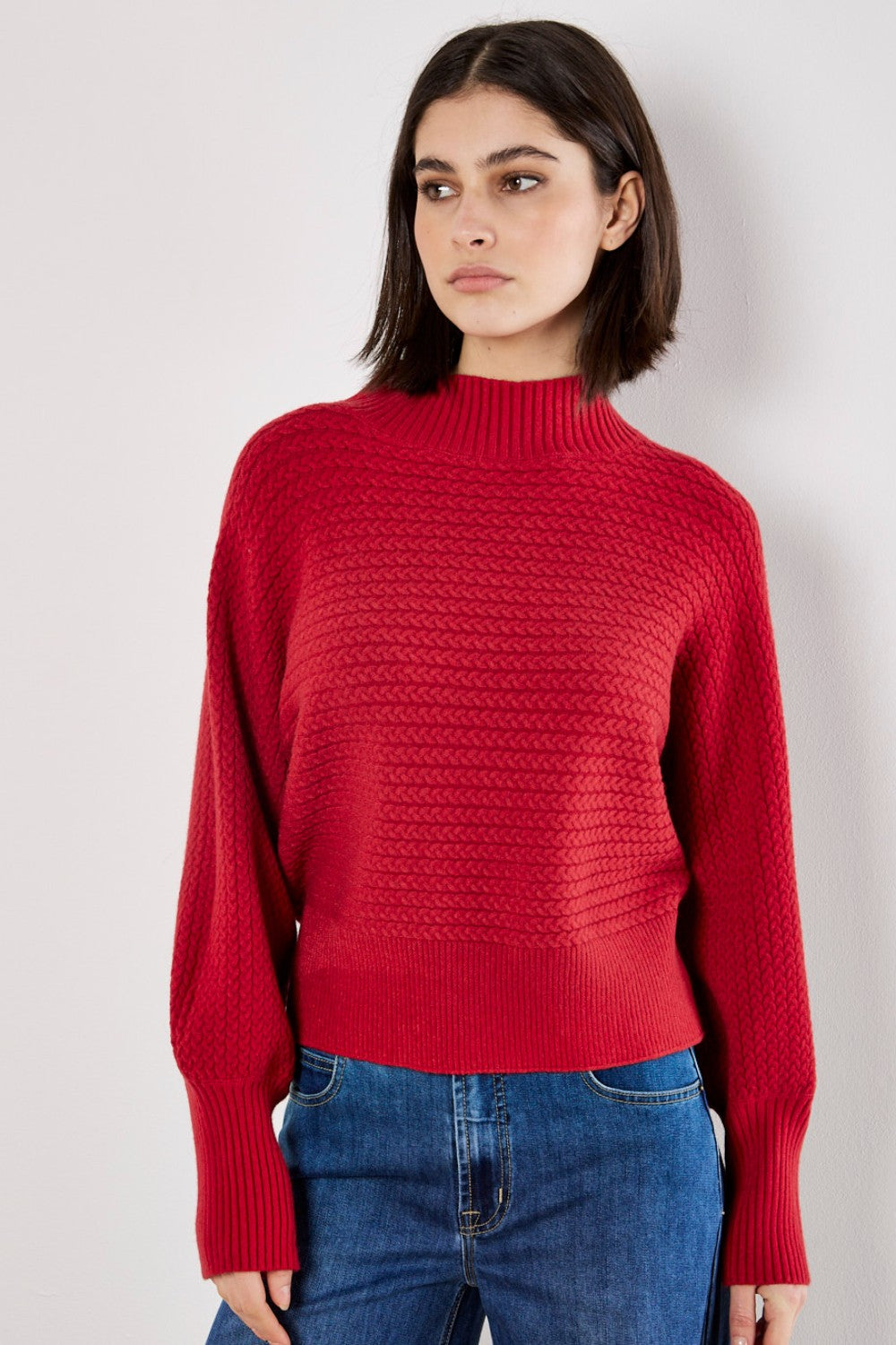 Woman wearing a red sweater and blue jeans against a plain background