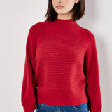 Woman wearing a red sweater and blue jeans against a plain background