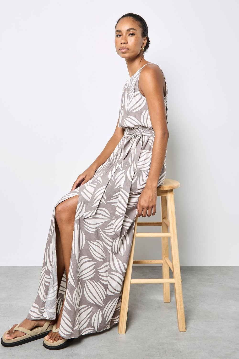 Woman in a long, patterned dress sitting on a wooden stool against a white background