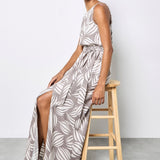 Woman in a long, patterned dress sitting on a wooden stool against a white background